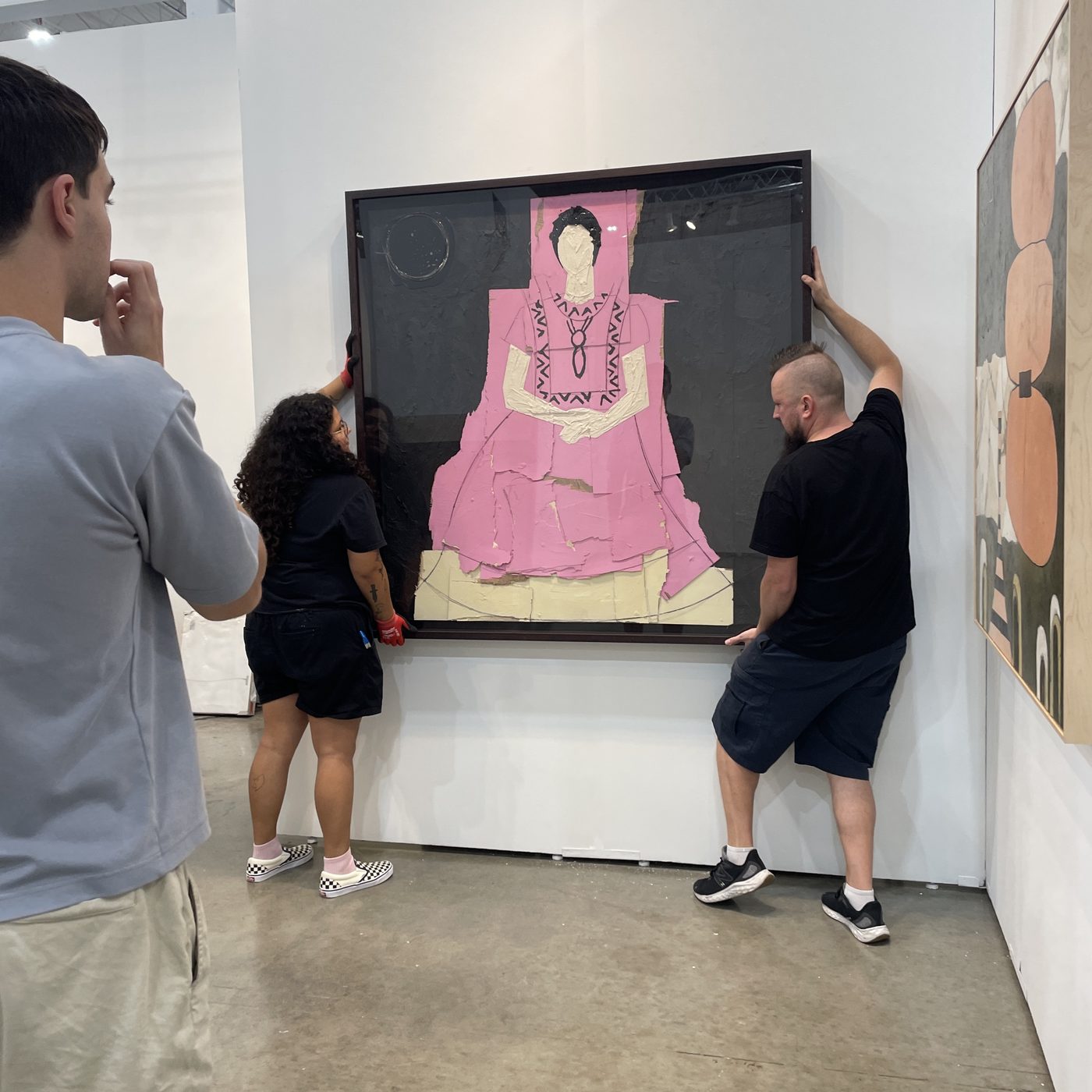 A three-person team lifting a large framed artwork into place